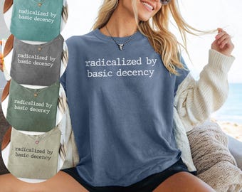 May include: A blue short-sleeved t-shirt featuring the white text "radicalized by basic decency" printed on the front. The shirt has a crew neckline and a relaxed fit. Additional color options are shown in circular insets on the left side.