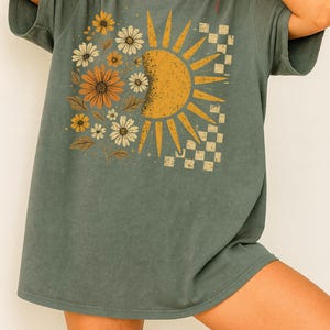 A woman wearing a gray t-shirt with a sun and flower design on it.