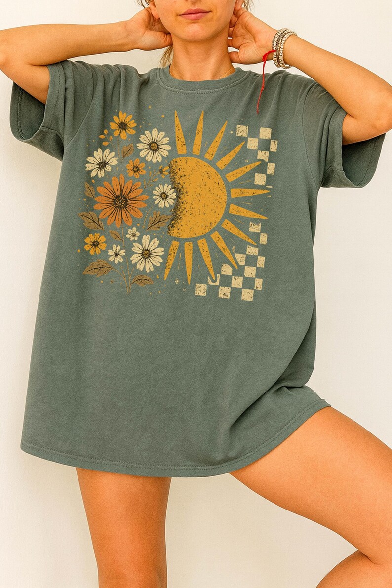 A woman wearing a gray t-shirt with a sun and flower design on it.