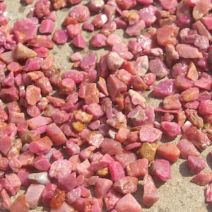 Può includere: Primo piano di un mucchio di pietre preziose di rubino rosa. Le pietre sono di varie dimensioni e forme, e sono tutte molto brillanti.