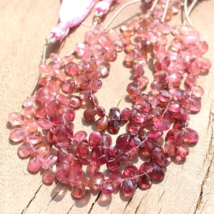 May include: A strand of pink and red gemstone beads, with a faceted, teardrop shape. The beads are strung on a silver wire and are ready to be used for jewelry making.