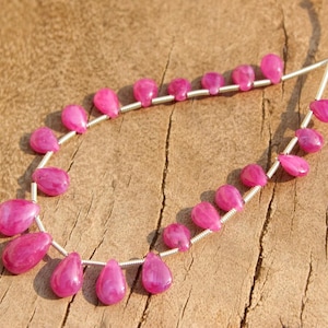 以下が含まれることがあります： 銀色のワイヤーにピンクの宝石ビーズが連なっています。ビーズは涙型で、光沢のある仕上げになっています。