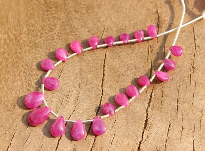 K&ouml;nnte beinhalten: Eine Kette aus rosafarbenen Edelsteinperlen, die auf einem Silberdraht aufgef&auml;delt sind. Die Perlen sind tropfenf&ouml;rmig und haben eine gl&auml;nzende Oberfl&auml;che.
