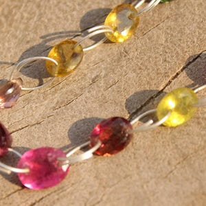 Pode incluir: Um bracelete de corrente de prata com contas de pedras preciosas rosa, amarelo e vermelho.