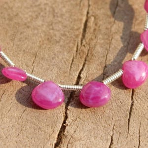 Può includere: Un filo di pietre preziose rosa a forma di cuore infilate su un filo d'argento.