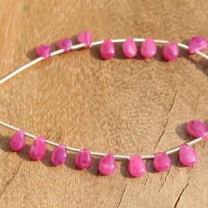 K&ouml;nnte beinhalten: Eine Reihe von rosafarbenen Edelsteinperlen in Tropfenform. Die Perlen sind auf einem Silberdraht aufgef&auml;delt und in einem Kreis angeordnet.