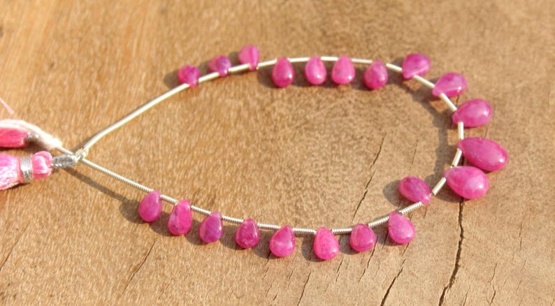 K&ouml;nnte beinhalten: Eine Reihe von rosafarbenen Edelsteinperlen in Tropfenform. Die Perlen sind auf einem Silberdraht aufgef&auml;delt und in einem Kreis angeordnet.