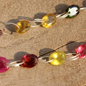 Pode incluir: Um colar de corrente de prata com pedras preciosas ovais coloridas. O colar apresenta pedras preciosas rosa, amarelas, verdes e marrons.