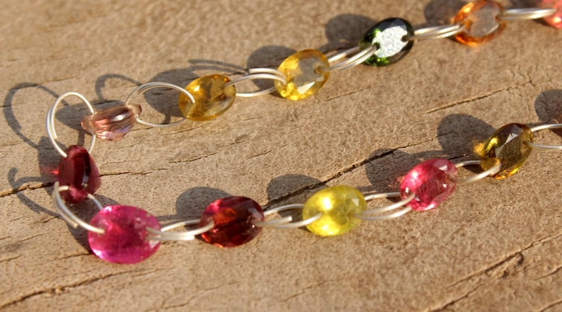 Pode incluir: Um colar de corrente de prata com pedras preciosas ovais coloridas. O colar apresenta pedras preciosas rosa, amarelas, verdes e marrons.