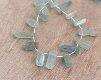 May include: A strand of light blue aquamarine gemstone beads, each bead is a rough, irregular, rectangular shape, strung on a silver wire.