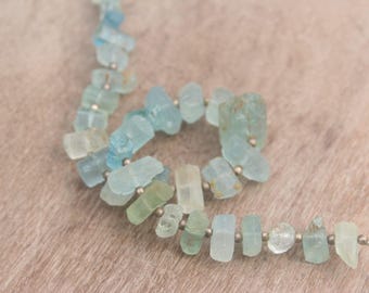 May include: A strand of aquamarine gemstone beads. The beads are irregular in shape, with a pale blue-green color and small silver-colored spacers. The beads are strung on a thin, silver-colored wire.