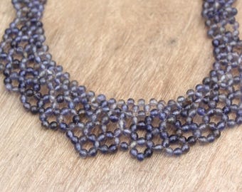 May include: A handcrafted necklace featuring a delicate, openwork design. The necklace is composed of small, round, dark blue beads, creating a layered effect. The beads are strung together to form a flexible, collar-style piece of jewelry.