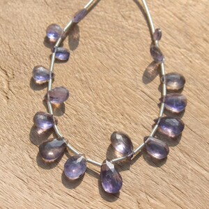 May include: A strand of purple amethyst gemstone beads in a teardrop shape. The beads are strung on a silver wire.