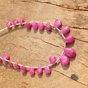 K&ouml;nnte beinhalten: Eine Reihe von rosafarbenen Edelsteinperlen in Tropfenform. Die Perlen sind auf einem Silberdraht aufgef&auml;delt.