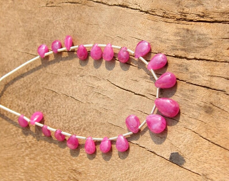 K&ouml;nnte beinhalten: Eine Reihe von rosafarbenen Edelsteinperlen in Tropfenform. Die Perlen sind auf einem Silberdraht aufgef&auml;delt.