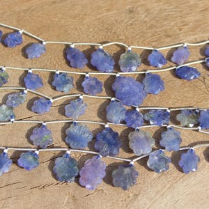 Puede incluir: Una hebra de cuentas de piedras preciosas azules en forma de flor, enhebradas en alambre plateado. Las cuentas son facetadas y tienen un color azul claro.