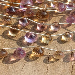 May include: A strand of faceted gemstone beads in shades of amethyst, peach, and amber. The beads are strung on silver wire.