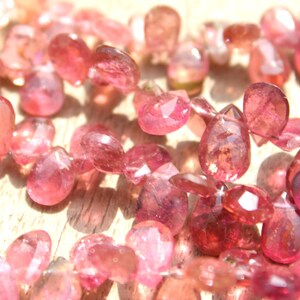 May include: A strand of pink gemstone beads, each bead is faceted and has a teardrop shape.