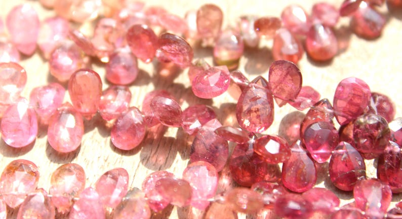 May include: A strand of pink gemstone beads, each bead is faceted and has a teardrop shape.
