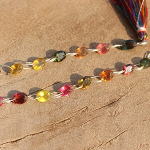 Pode incluir: Um colar de pedras preciosas multicoloridas com uma corrente de prata e um tassel colorido. O colar apresenta pedras preciosas redondas e facetadas em tons de rosa, verde, amarelo e marrom.