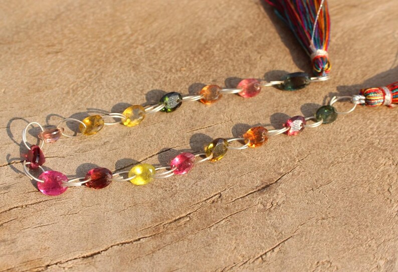 Pode incluir: Um colar de pedras preciosas multicoloridas com uma corrente de prata e um tassel colorido. O colar apresenta pedras preciosas redondas e facetadas em tons de rosa, verde, amarelo e marrom.