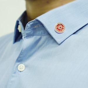 May include: A light blue dress shirt with a white button and a red and gold flower pin on the collar.