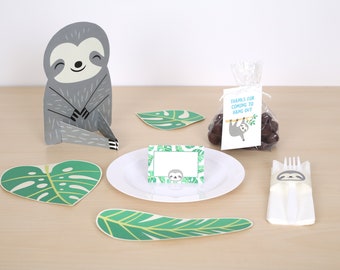 May include: A sloth-themed party table setting with a grey cardboard sloth cutout, green leaf placemats, a white plate with a sloth-themed place card, a clear bag of chocolate treats with a sloth-themed tag that says "Thanks for coming to hang out", and a white plastic fork with a sloth-themed napkin wrapper.