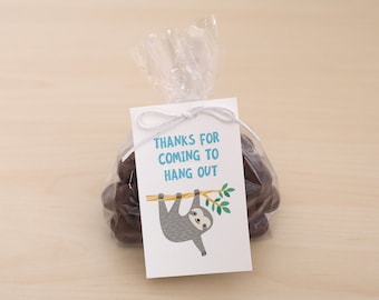 May include: A white gift tag with blue text that reads "Thanks for coming to hang out". A cartoon sloth hangs from a branch with green leaves. The tag is tied to a clear plastic bag filled with chocolate candies.