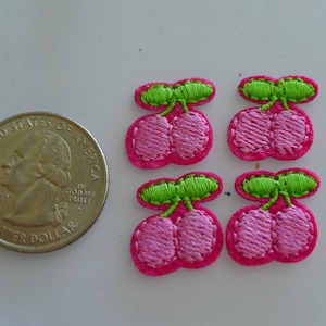 May include: Four pink felt cherries with green felt stems and leaves. The cherries are about the size of a US quarter.