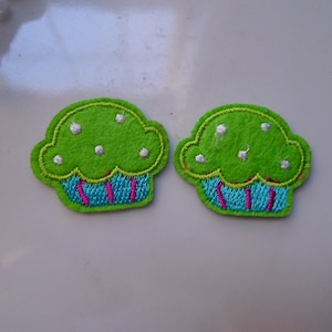 May include: Two green felt cupcake appliques with white frosting and blue and pink icing.