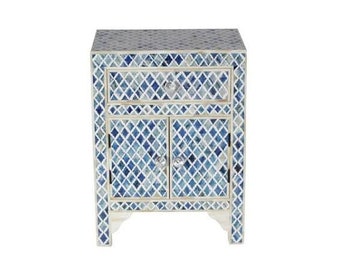 May include: A small blue and white nightstand with a single drawer and two doors. The nightstand is made of inlaid bone and has a geometric pattern.