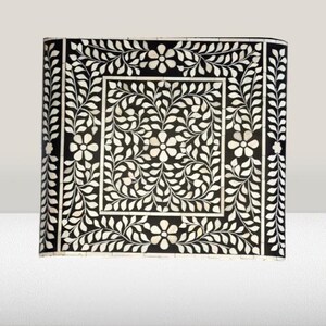 May include: A black and white square tray with a floral design made of mother of pearl inlay. The tray has a border of leaves and flowers.