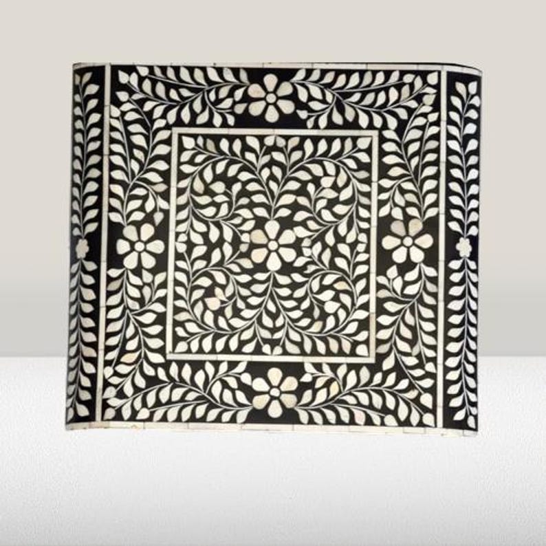May include: A black and white square tray with a floral design made of mother of pearl inlay. The tray has a border of leaves and flowers.