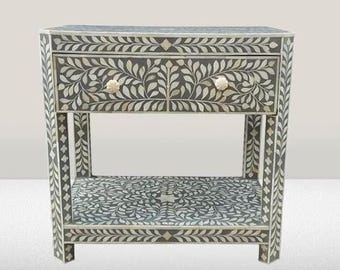 May include: A gray bone inlay console table with a floral design. The table has two drawers and a lower shelf. The drawers have bone inlay knobs.