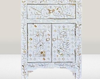May include: White nightstand with a floral design made of mother of pearl inlay. The nightstand has a single drawer and two doors.