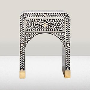 May include: Black and white nightstand with a floral inlay design and a single drawer. The nightstand has a gold base and an arched top.
