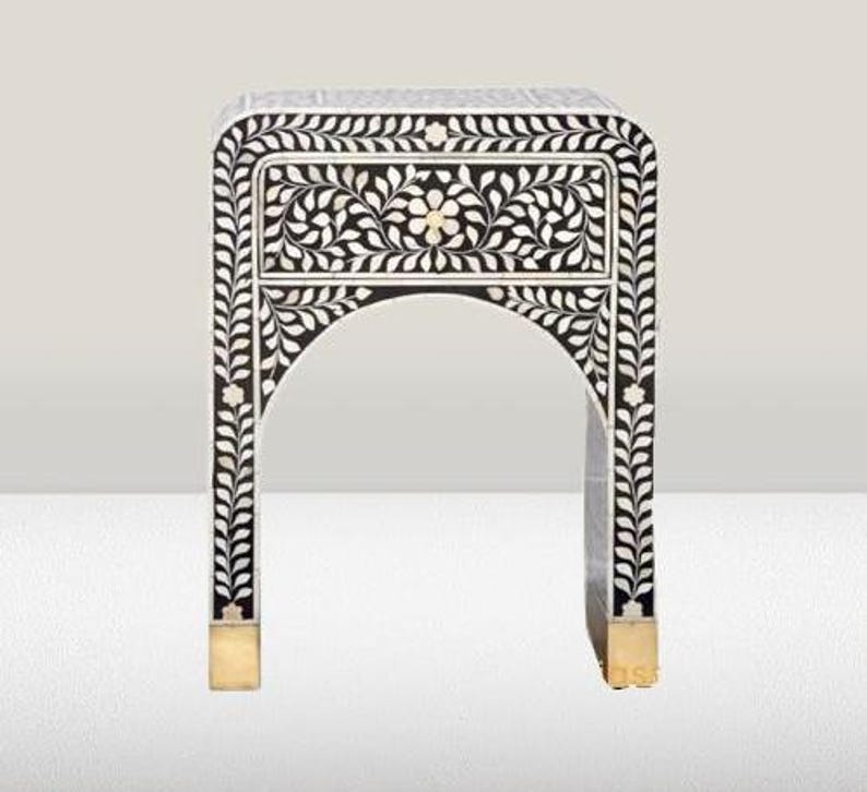 May include: Black and white nightstand with a floral inlay design and a single drawer. The nightstand has a gold base and an arched top.