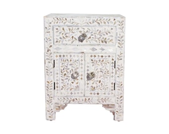 May include: White nightstand with a floral inlay design. The nightstand has a single drawer and two doors. The doors have a floral design and a silver knob.
