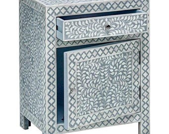 May include: A small, light blue nightstand with a white floral pattern. It has a single drawer and a cabinet door with a floral design. The nightstand is made of wood and has a distressed finish.