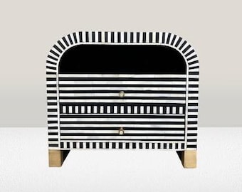 May include: A black and white striped nightstand with two drawers and gold accents. The nightstand has a curved top and is made of wood.
