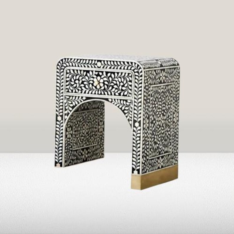 May include: A black and white bone inlay end table with a single drawer and a brass base. The table features a floral design.