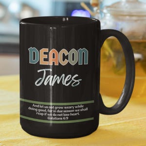 May include: Black ceramic mug with a white inscription that reads "DEACON James" and a quote from Galatians 6:9. The mug has a white handle.