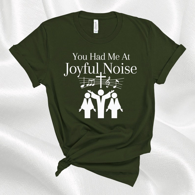 May include: A green t-shirt with the text "You Had Me At Joyful Noise" in white. The text is accompanied by a graphic of three people singing with musical notes and a cross.