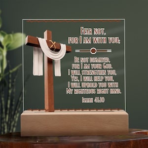May include: A wooden cross with a white cloth draped over it. The cross is on a clear acrylic plaque with the text "FEAR NOT, FOR I AM WITH YOU: BE NOT DISMAYED, FOR I AM YOUR GOD. I WILL STRENGTHEN YOU, YES, I WILL HELP YOU, I WILL UPHOLD YOU WITH MY RIGHTEOUS RIGHT HAND. ISAIAH 41:10". The plaque is on a wooden base.