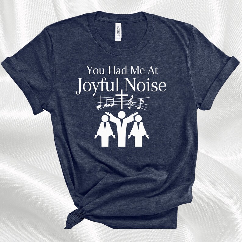 May include: A navy blue t-shirt with white text that reads "You Had Me At Joyful Noise". The text is accompanied by a graphic of three people singing with musical notes and a cross above them.