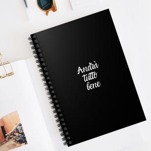 May include: Black spiral bound notebook with the text "Andrà tutto bene" in white cursive writing.