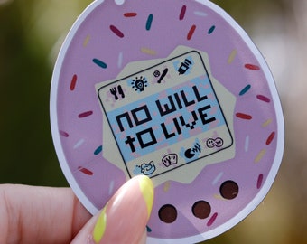 May include: Pink and white digital pet toy with a screen that reads "NO WILL TO LIVE". The toy is covered in colorful sprinkles.