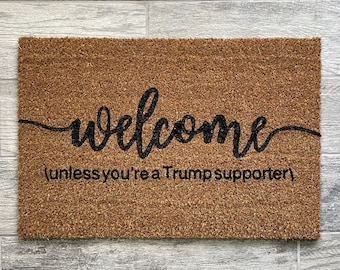 May include: A brown coir doormat with the word "welcome" written in black cursive script. Below the word "welcome" is the text "(unless you're a Trump supporter)".