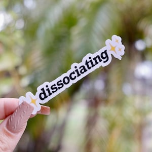 May include: White sticker with the text "dissociating" in black letters and two yellow stars on either side.