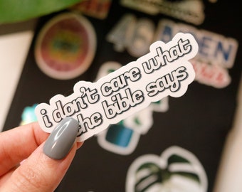 May include: White sticker with the text "i don't care what the bible says" in a bold, black outline. The sticker has a glossy finish and is slightly curved.